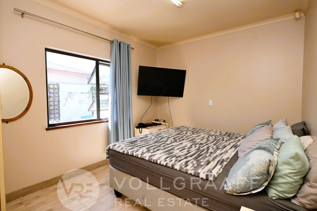 A functional bedroom featuring tiled flooring, neutral wall finishes, and an aluminium-framed window.