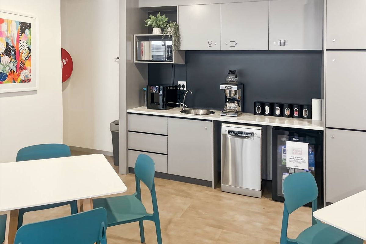 A modern office kitchenette featuring grey cabinetry, a stainless steel sink, integrated dishwasher, and built-in microwave, providing a functional break area for staff.