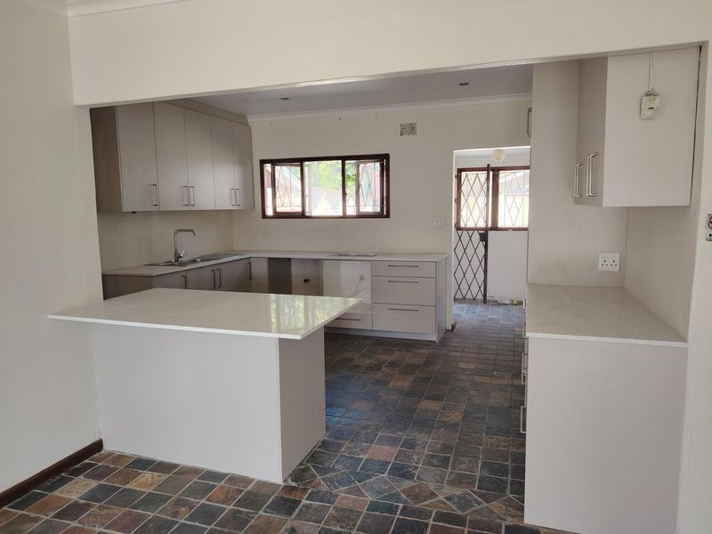 A clean, open-plan kitchen featuring modern cabinetry, stone countertops, and durable tiled flooring, offering a functional and bright workspace.