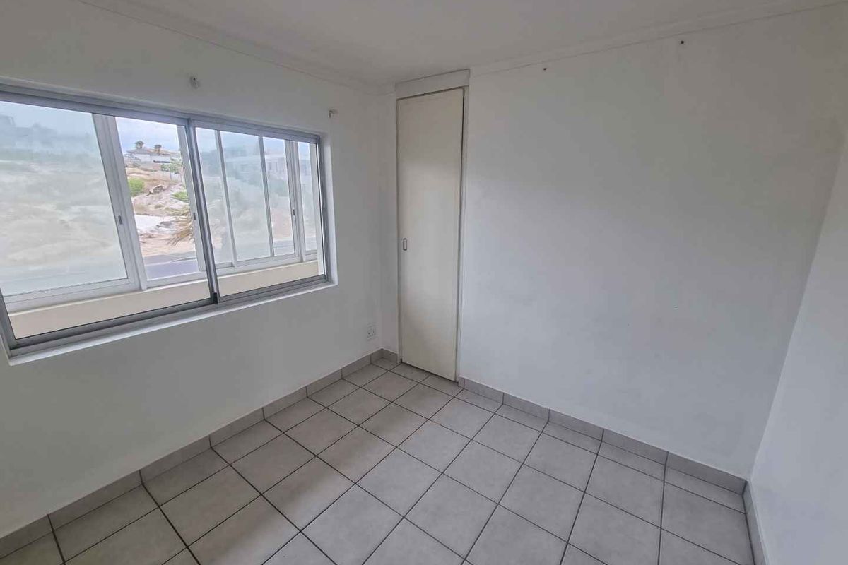 An empty bedroom featuring tiled flooring, a built-in cupboard, and a sliding window with natural light.