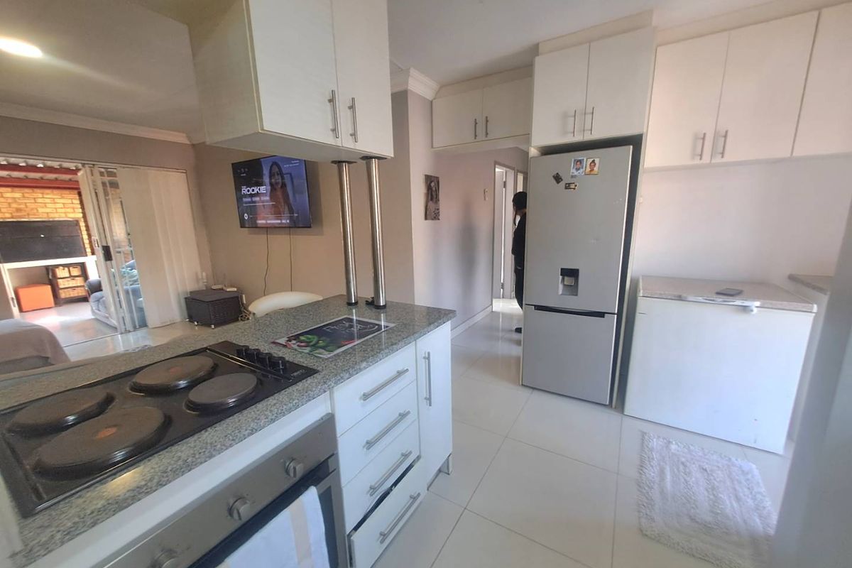 A functional kitchen featuring granite countertops, built-in cabinetry, an electric hob, and an oven, with tiled flooring and a view into the adjacent living area.