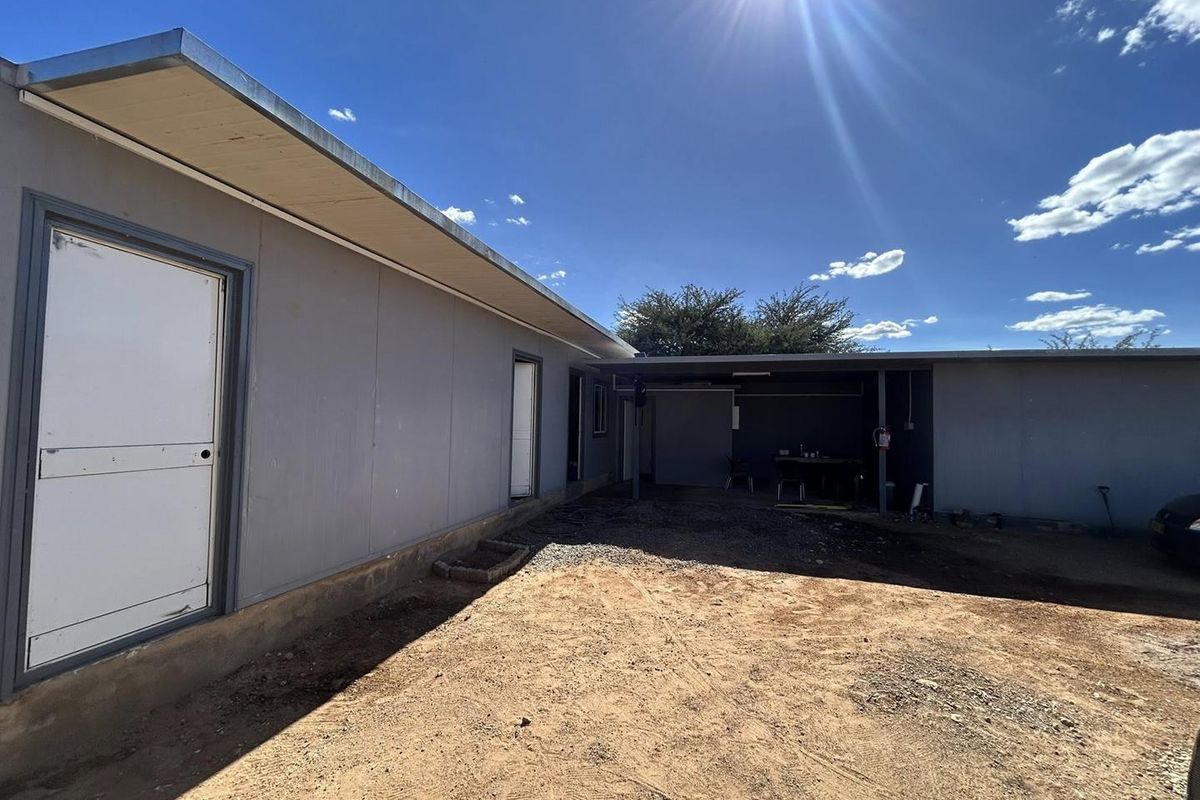 Rear exterior view of the property featuring a covered patio area and unpaved ground, offering potential for landscaping and outdoor improvement.
