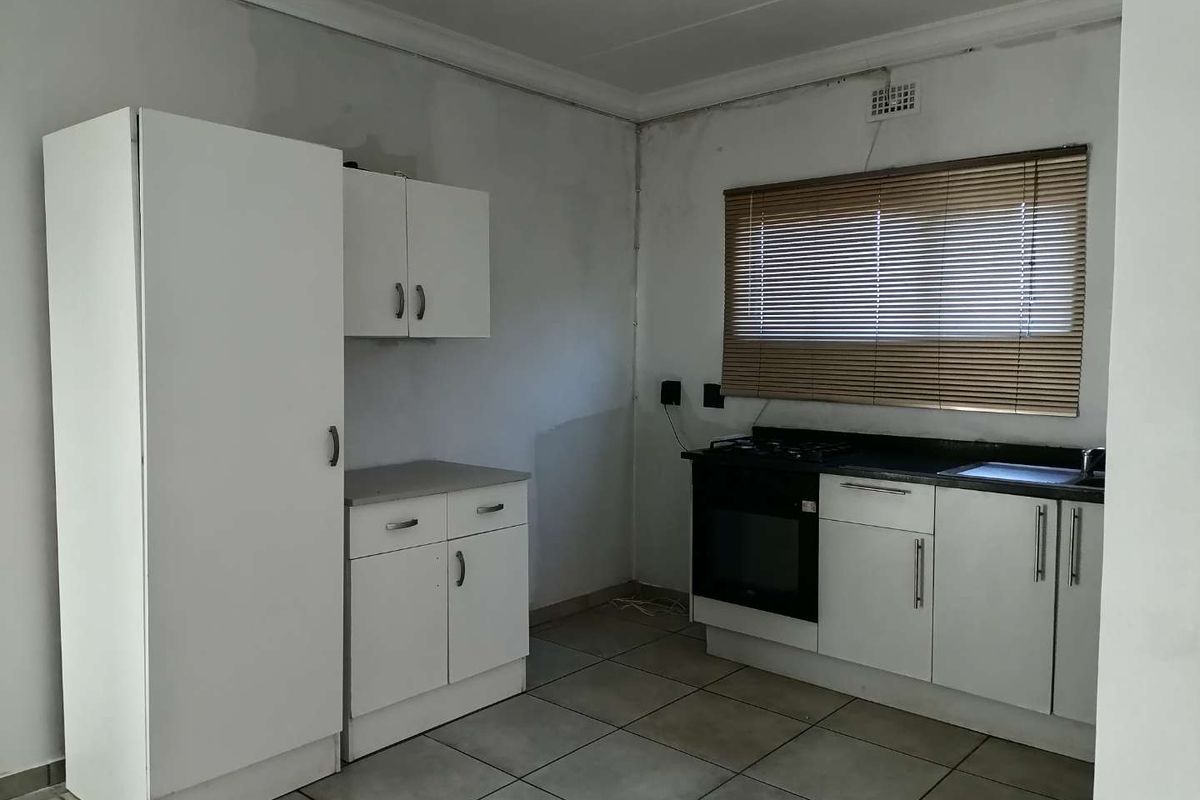 A functional kitchen featuring white cabinetry, a built-in oven, and a gas hob, with tiled flooring and a window with fitted blinds.
