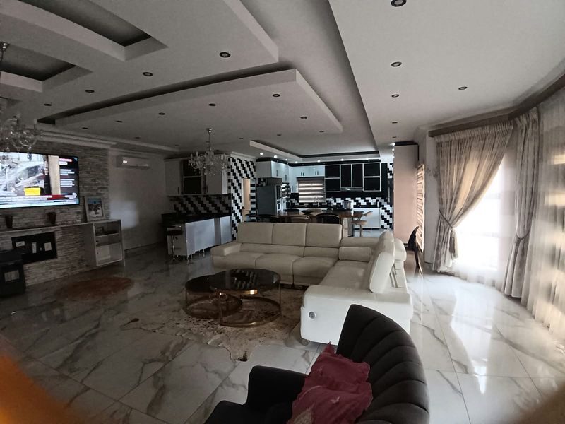 Spacious open-plan living and kitchen area featuring modern marble-look flooring, a stone-clad feature wall, and a contemporary recessed ceiling design with integrated lighting.