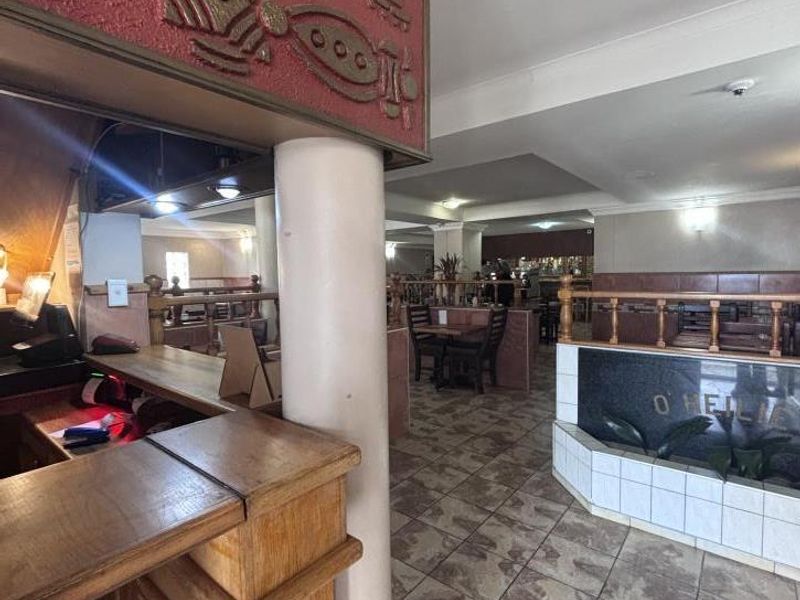 A commercial bar area featuring a built-in wooden counter, decorative wall detailing, tiled flooring, and a partitioned seating layout.