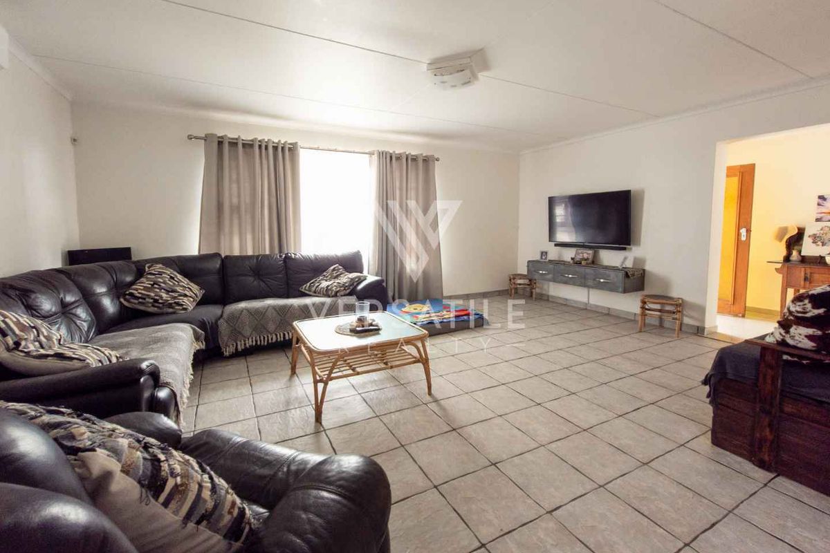 Spacious living room featuring neutral tiled flooring and a wall-mounted television unit, offering a comfortable and functional layout for relaxation.