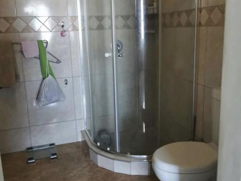 A functional bathroom featuring a corner shower enclosure and a standard toilet with neutral wall and floor tiling.