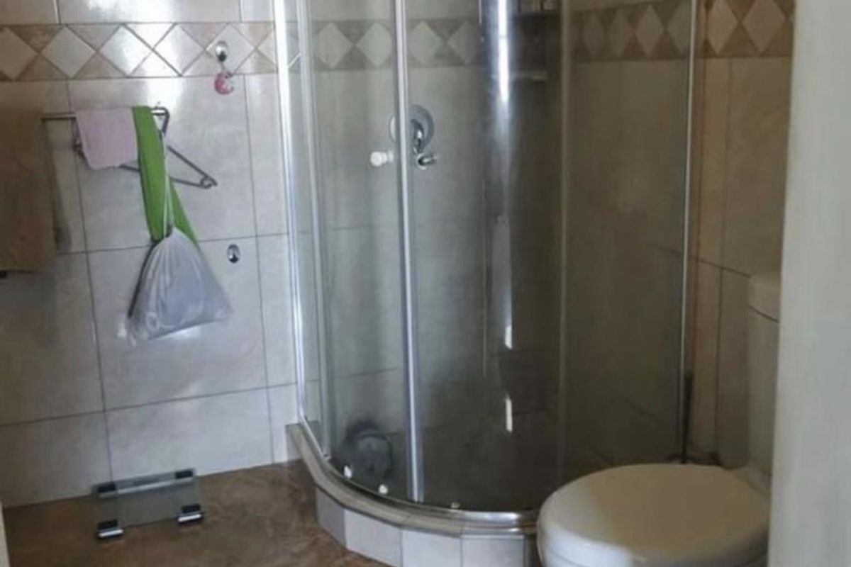 A functional bathroom featuring a corner shower enclosure and a standard toilet with neutral wall and floor tiling.