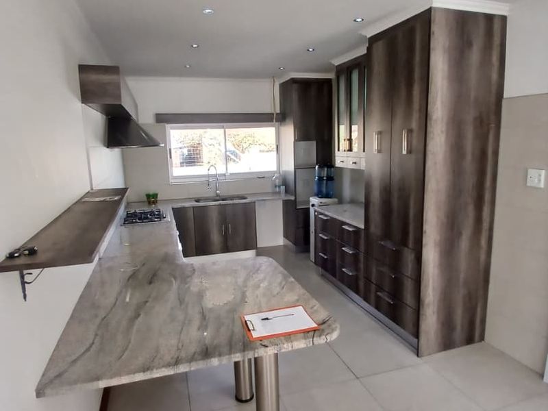 Modern kitchen featuring dark wood cabinetry, stone countertops, a gas hob, extractor fan, and tiled flooring with recessed lighting.
