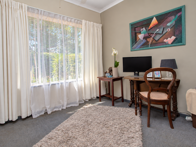 A bedroom featuring carpet flooring, cove cornice, and a large window fitted with security bars, providing natural light.