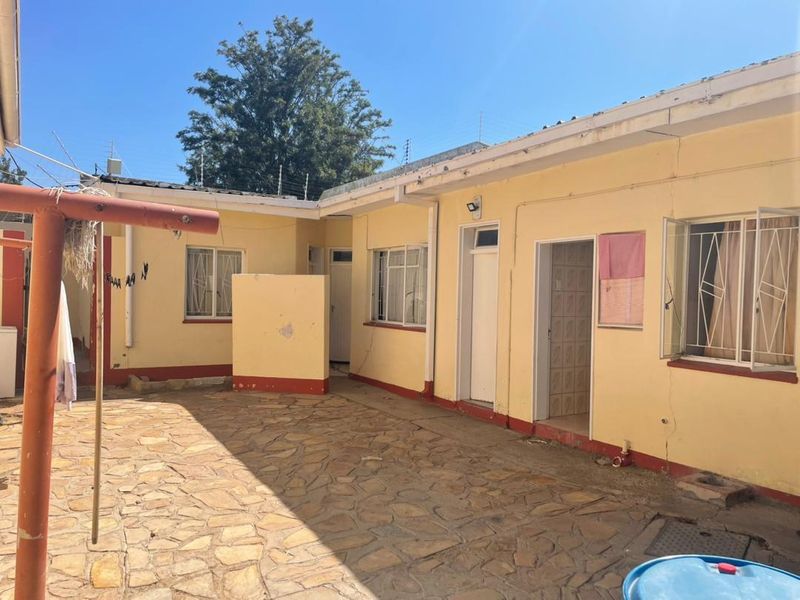 Rear courtyard area featuring stone paving, security bars on windows, and perimeter electric fencing, showing signs of wear and maintenance requirements.
