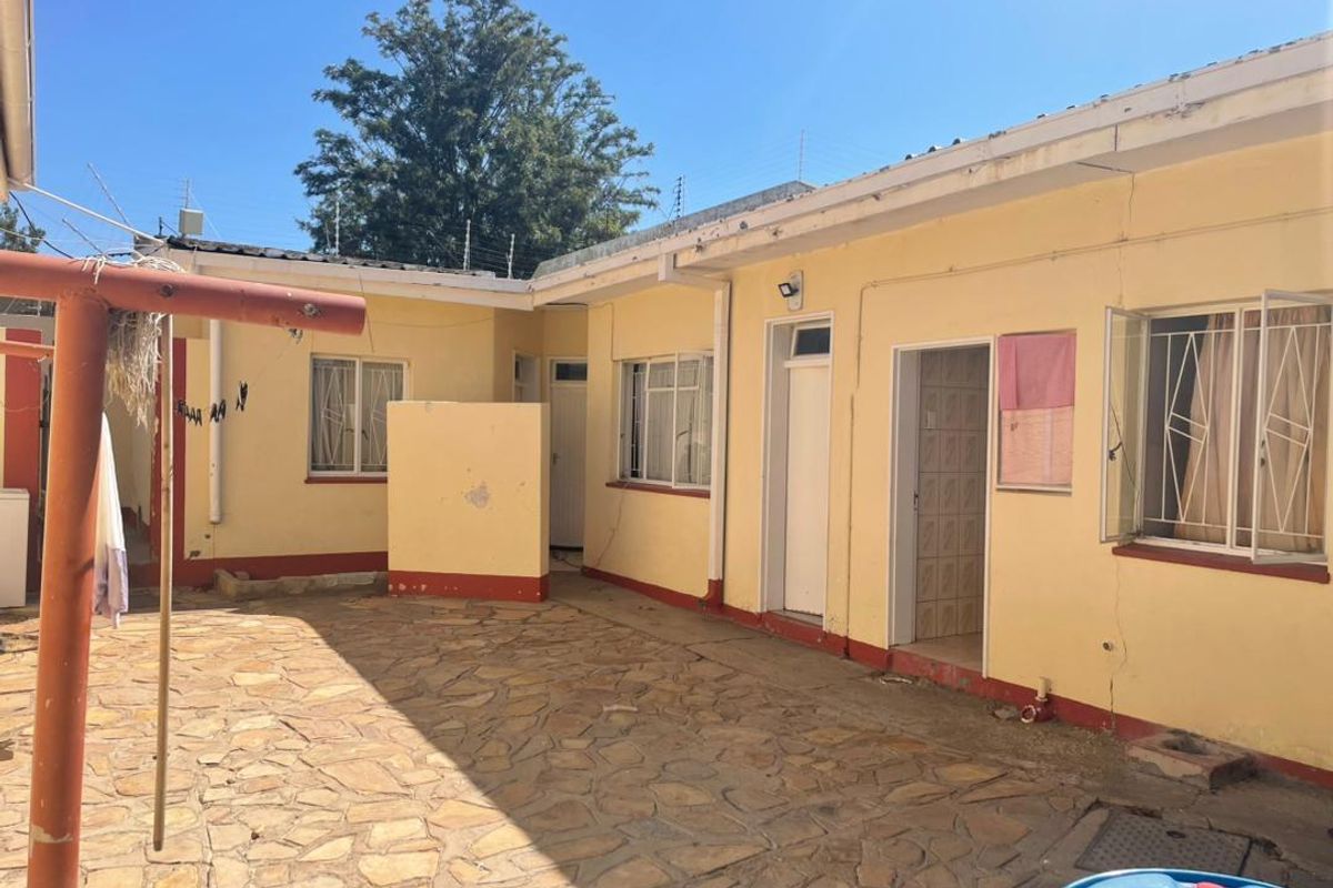 Rear courtyard area featuring stone paving, security bars on windows, and perimeter electric fencing, showing signs of wear and maintenance requirements.