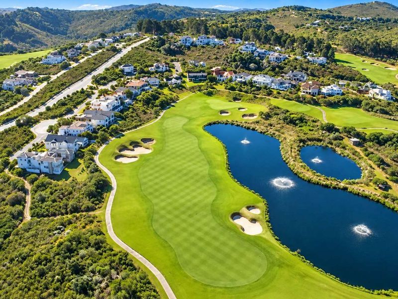 Aerial view of a residential estate featuring a well-maintained golf course, water features, and surrounding natural landscape.