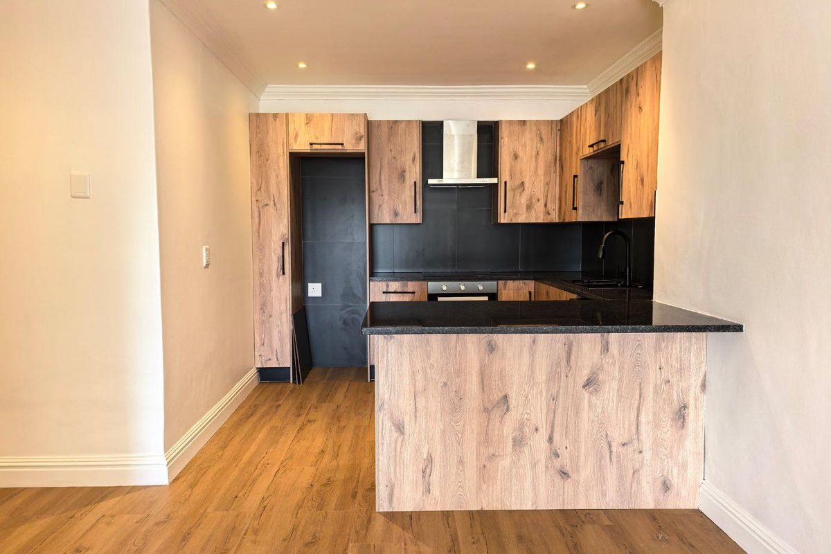 Modern kitchen featuring wood-look cabinetry, black granite countertops, built-in oven, extractor fan, and sleek black fixtures in an open-plan layout.