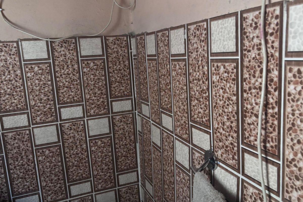 A bathroom corner featuring decorative textured wall tiling and a fixed towel rail, requiring minor maintenance to address exposed wiring.