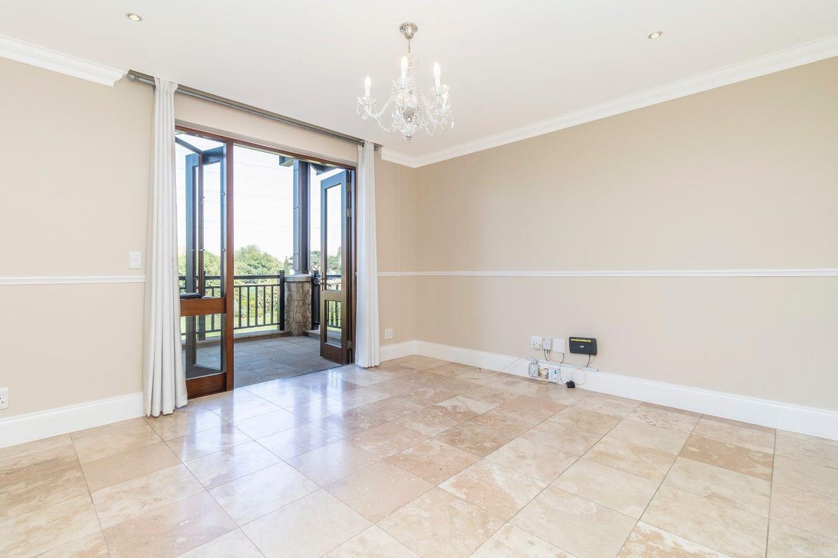 Bright living area featuring neutral tiled flooring, crown molding, a decorative chandelier, and double doors opening onto a private balcony.