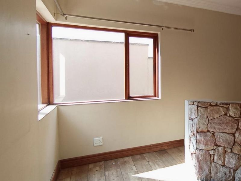 An empty bedroom featuring timber-look tiled flooring, a unique stone-clad feature wall, and timber-framed windows with a curtain rod installed.
