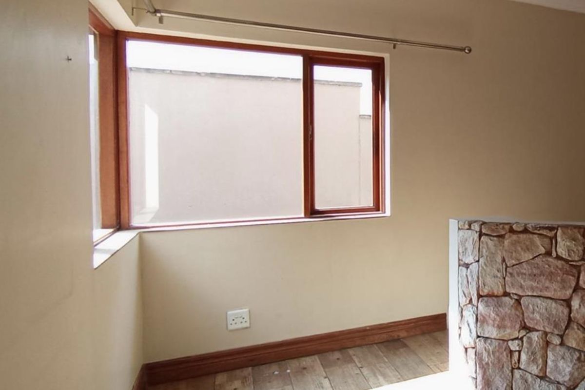 An empty bedroom featuring timber-look tiled flooring, a unique stone-clad feature wall, and timber-framed windows with a curtain rod installed.