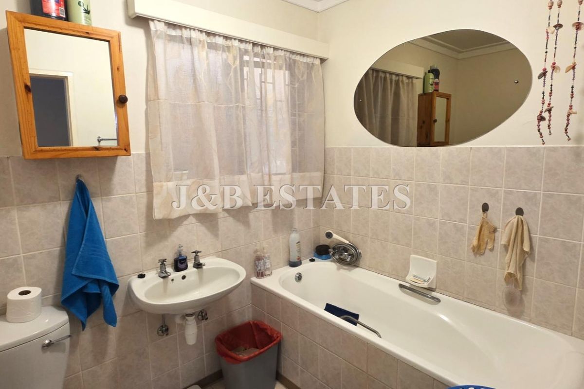 A functional bathroom featuring a standard bathtub, wall-mounted basin, and toilet with neutral wall tiling.