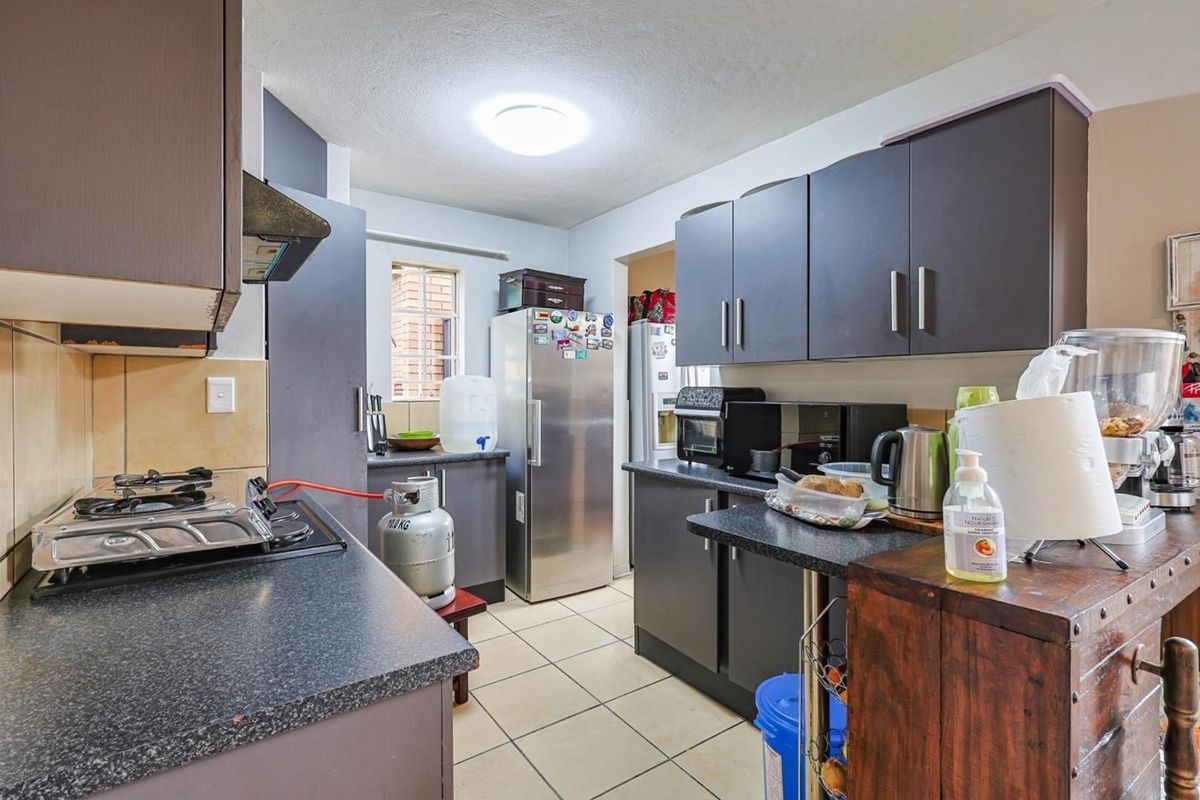 Functional kitchen featuring dark cabinetry, laminate countertops, tiled flooring, and a built-in gas hob with extractor fan.