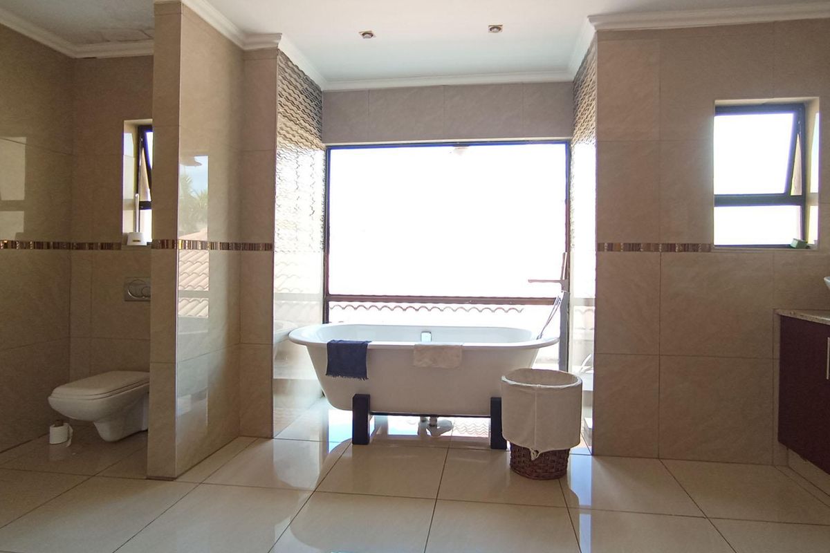 Spacious bathroom featuring a freestanding bathtub, wall-mounted toilet, and a modern vanity with a vessel sink, finished with neutral floor-to-ceiling tiling.