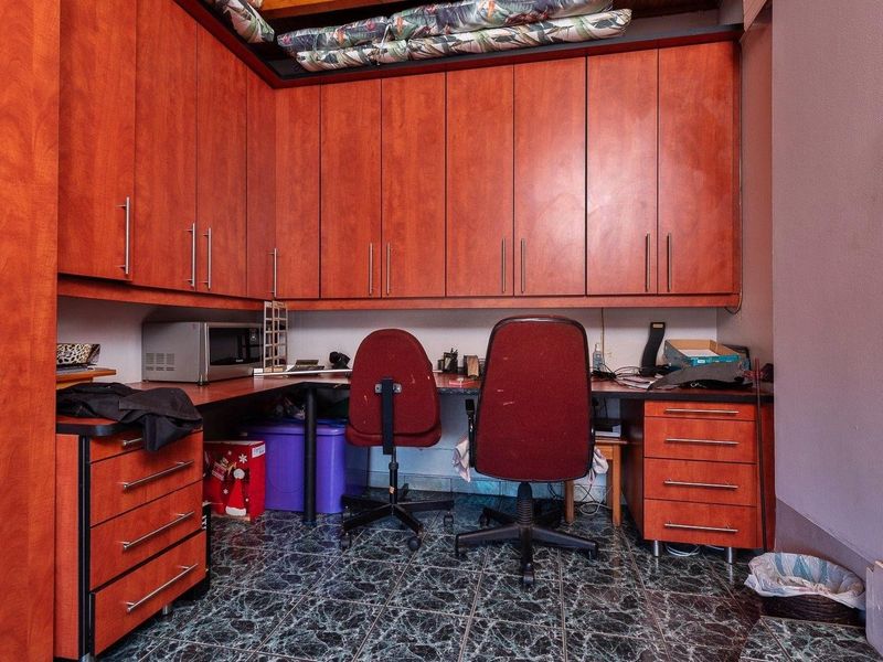 A functional home office space featuring extensive built-in cabinetry, a wrap-around desk workspace, and durable tiled flooring.
