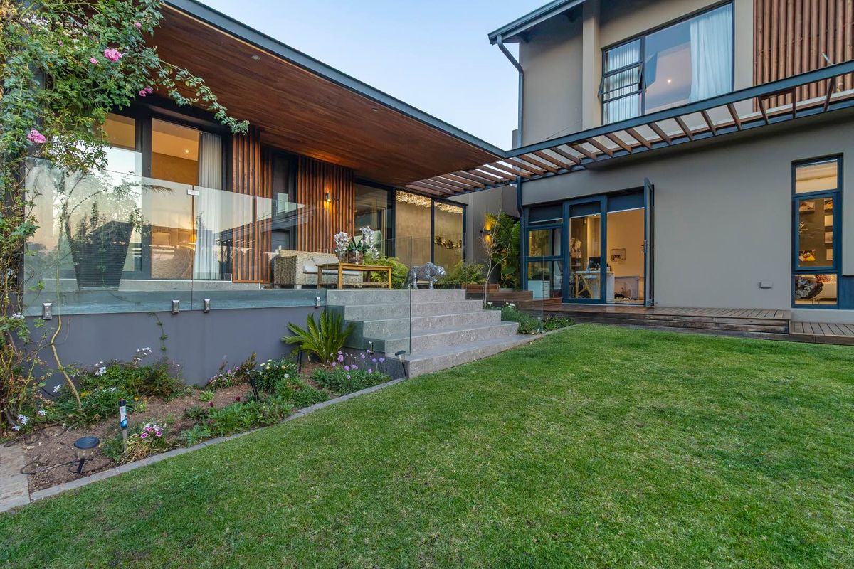 A modern rear exterior featuring a landscaped garden, timber decking, a covered patio area with a glass balustrade, and contemporary architectural finishes.