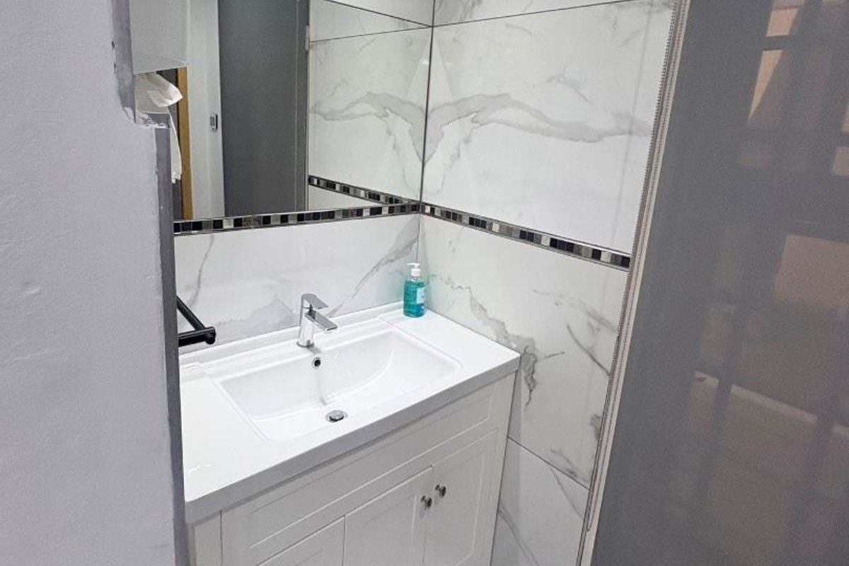 Modern bathroom featuring marble-look wall and floor tiles, a white vanity cabinet with integrated sink, and a large wall mirror.