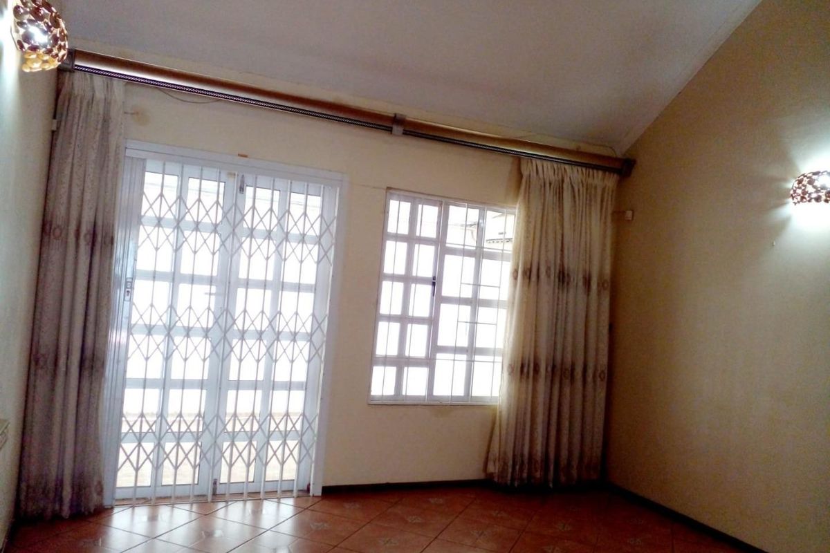 An empty living room featuring tiled flooring, a security gate, and a sliding door leading to an outdoor area.