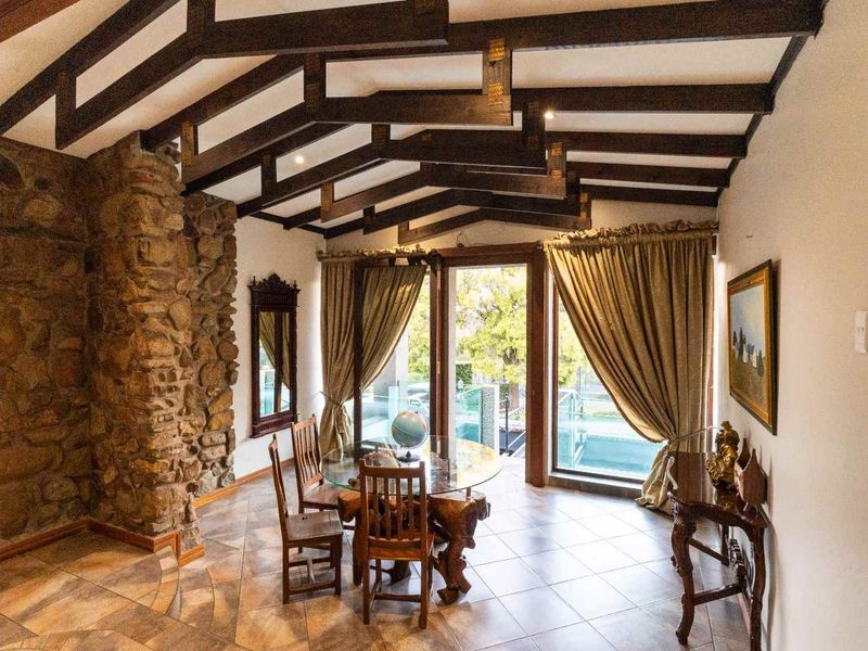 Dining area featuring a striking stone feature wall, exposed timber ceiling beams, and large sliding glass doors providing access to the outdoor pool area.