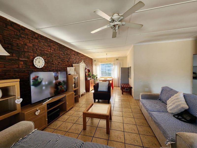 Spacious living area featuring an exposed brick feature wall, tiled flooring, and a ceiling fan, offering a comfortable and functional layout.