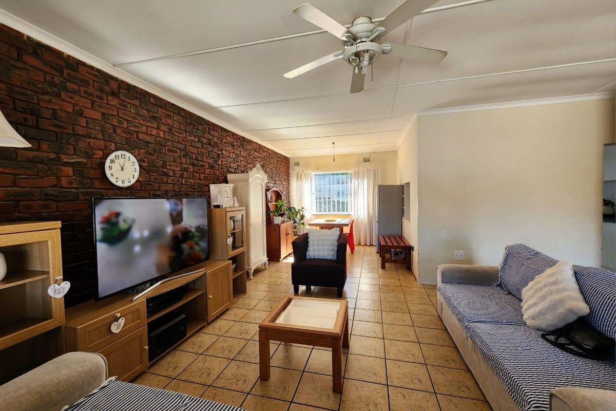 Spacious living area featuring an exposed brick feature wall, tiled flooring, and a ceiling fan, offering a comfortable and functional layout.