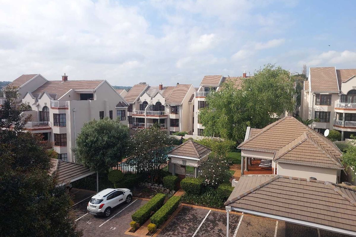 An elevated aerial view of an apartment complex featuring multiple residential buildings, paved parking areas, carports, and well-maintained communal garden spaces.