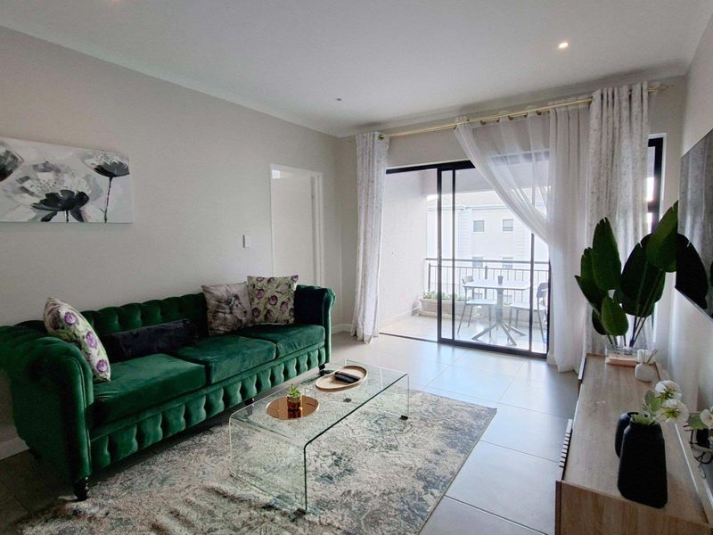 A bright and modern living room featuring tiled flooring, recessed lighting, and direct access to a private balcony through sliding glass doors.