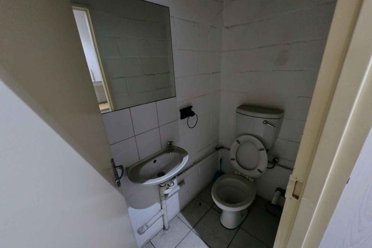 A compact industrial-style bathroom featuring a wall-mounted basin, toilet, and mirror, requiring cosmetic updates to improve its overall condition and appearance.