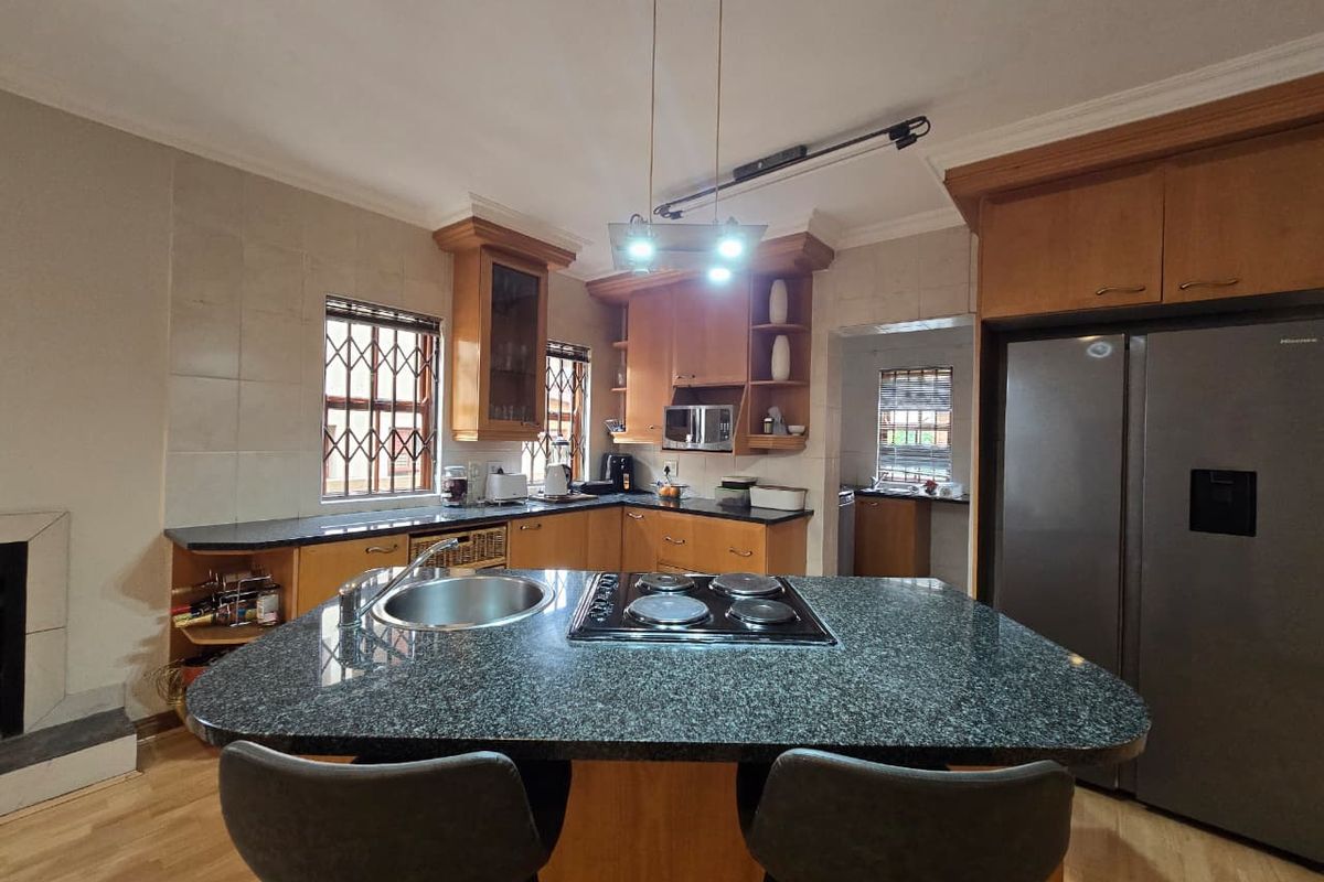 Functional kitchen featuring wooden cabinetry, granite countertops, a central island with a built-in hob and sink, and integrated appliances.