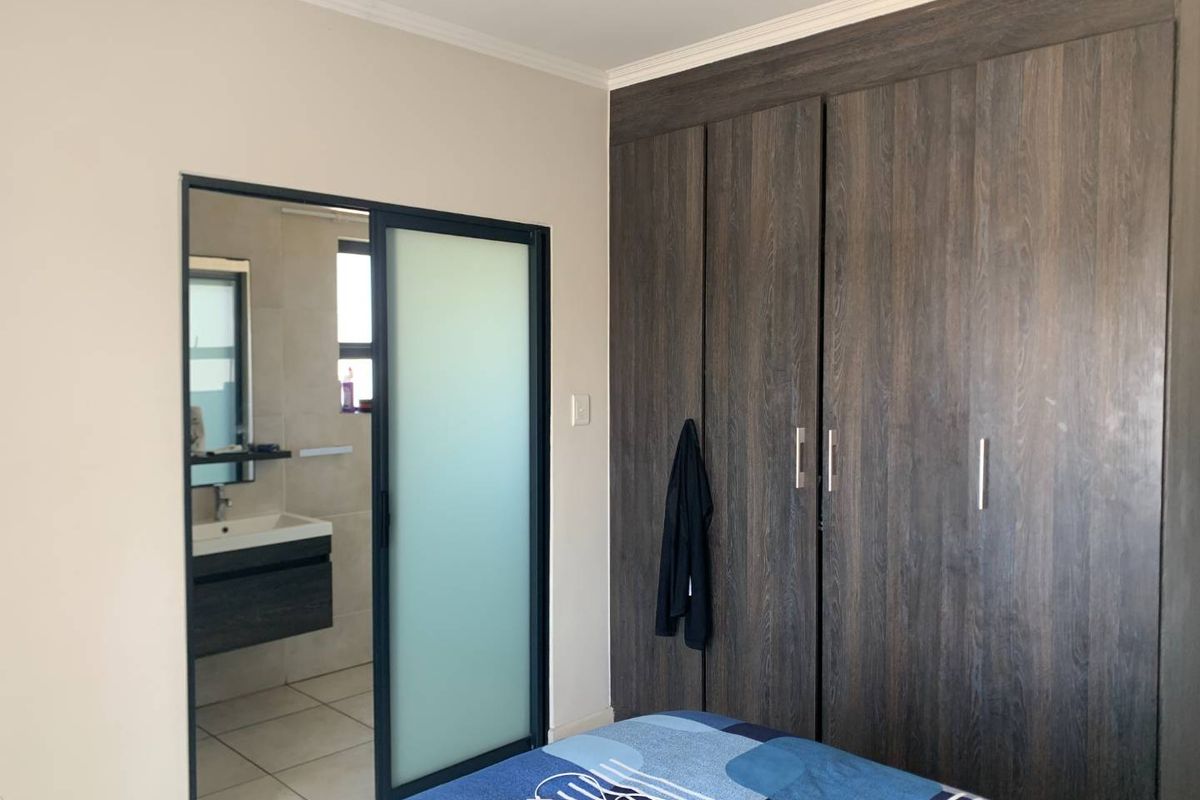 Bedroom featuring built-in dark wood-grain wardrobes and an adjoining en-suite bathroom with a sliding frosted glass door.