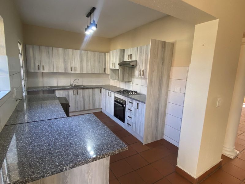 Spacious kitchen featuring light wood-grain cabinetry, granite countertops, built-in oven, gas hob, and tiled flooring, offering a functional and open layout.