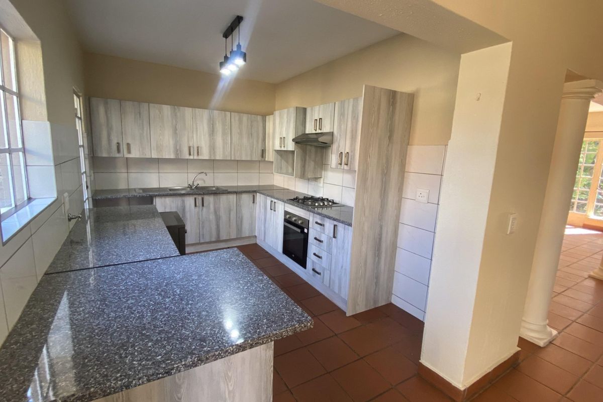 Spacious kitchen featuring light wood-grain cabinetry, granite countertops, built-in oven, gas hob, and tiled flooring, offering a functional and open layout.