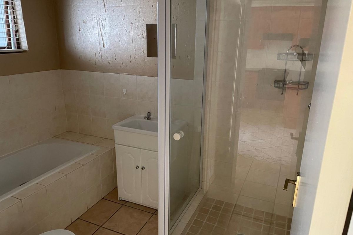 A functional bathroom featuring a built-in bathtub, separate glass shower enclosure, and a vanity cabinet with tiled flooring and wall finishes.