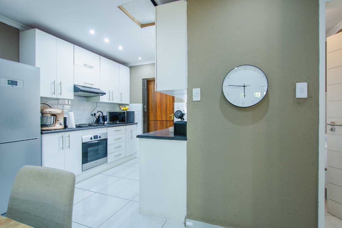 A modern kitchen featuring white cabinetry, dark countertops, a built-in oven, and a sleek extractor fan, complemented by tiled flooring and recessed lighting.