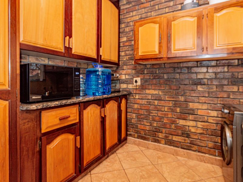 A functional scullery area featuring warm-toned wooden cabinetry, granite countertops, and an exposed brick feature wall, providing ample storage and workspace.
