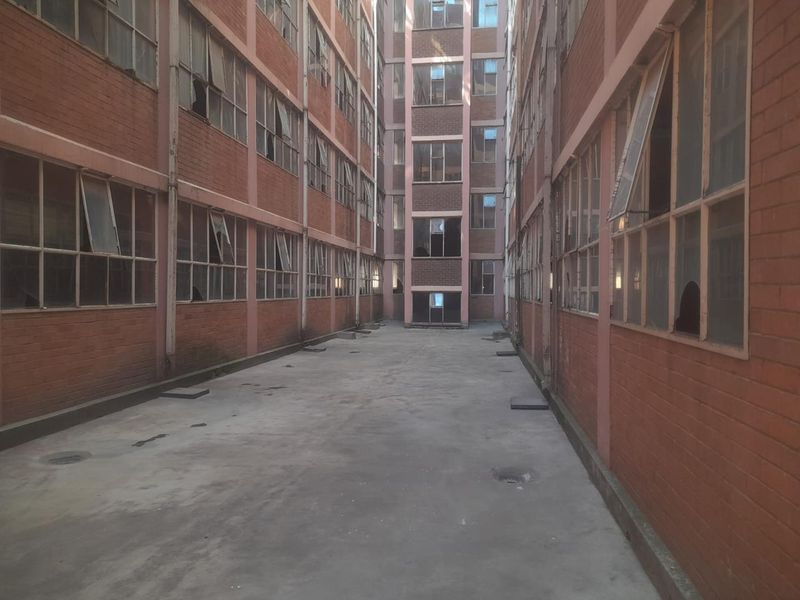 A view of the rear exterior courtyard featuring brick building facades with multiple steel-framed windows showing signs of wear and damage.