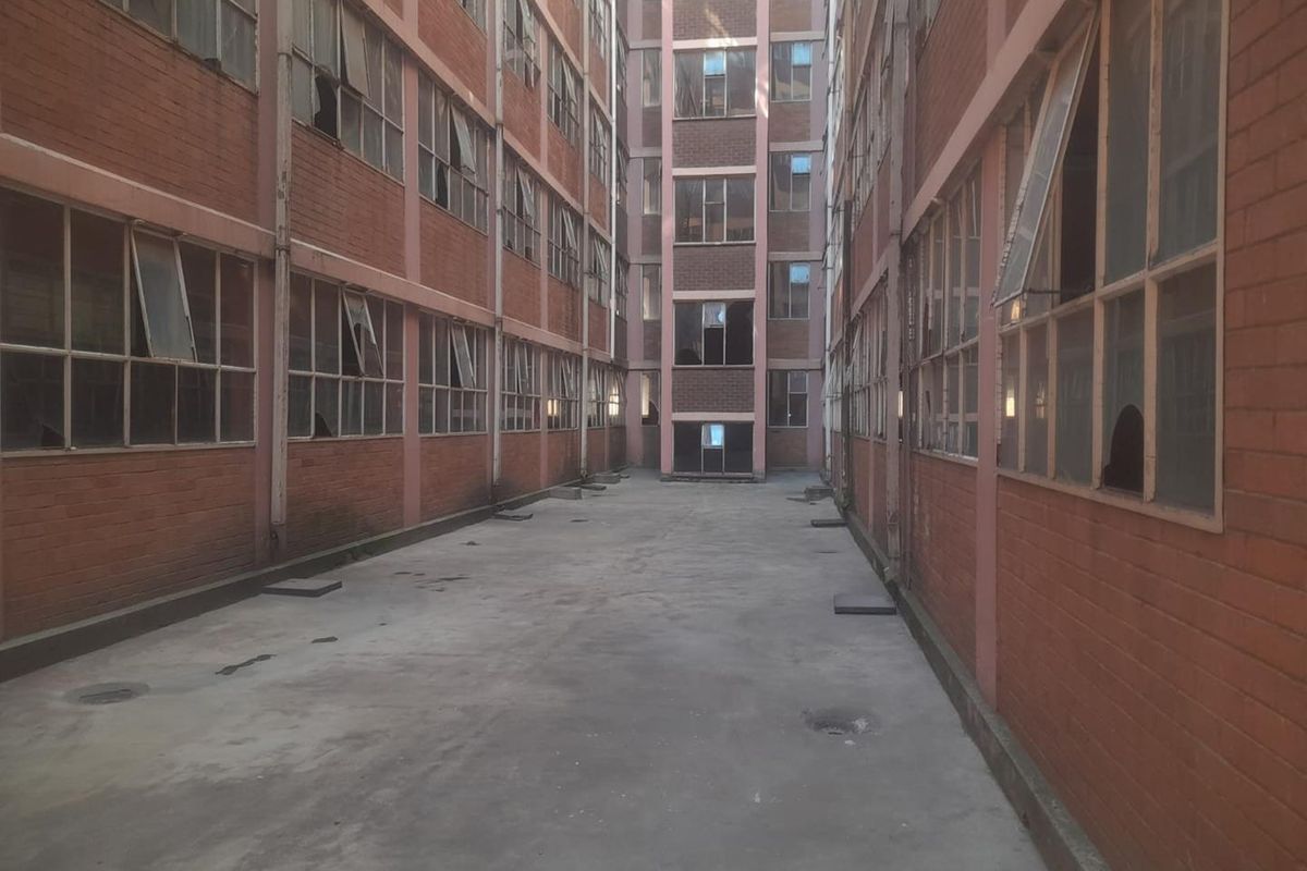 A view of the rear exterior courtyard featuring brick building facades with multiple steel-framed windows showing signs of wear and damage.