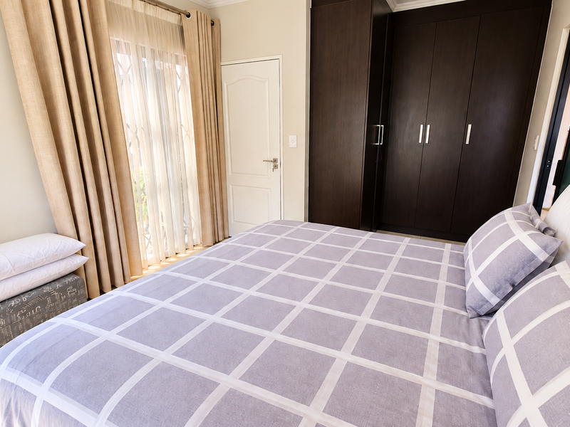 A well-maintained bedroom featuring dark wood built-in cupboards, neutral wall finishes, and a sliding door with a security gate providing natural light.