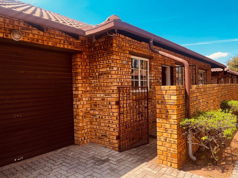 Front elevation of a face brick townhouse featuring a single garage, paved driveway, and secure gated entrance.