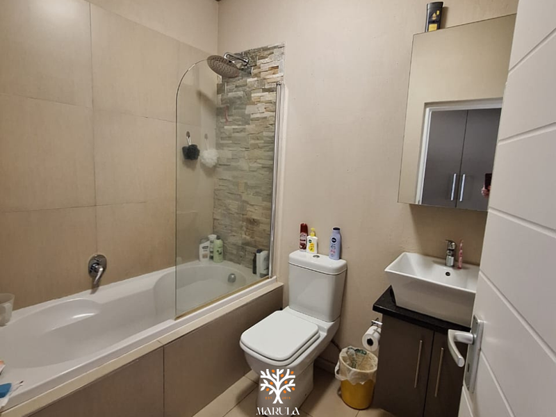 A functional bathroom featuring a bathtub with a glass screen, stone accent wall, modern vessel sink, and vanity storage.