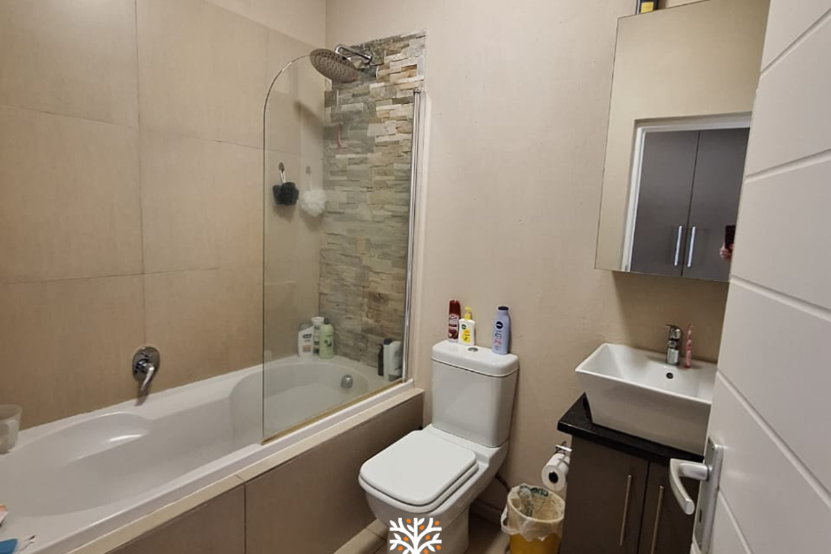 A functional bathroom featuring a bathtub with a glass screen, stone accent wall, modern vessel sink, and vanity storage.