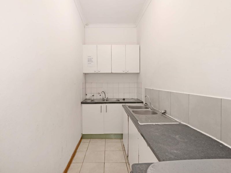 A functional scullery or utility area featuring double stainless steel sinks, laminate countertops, and ample built-in cabinetry with tiled splashbacks.