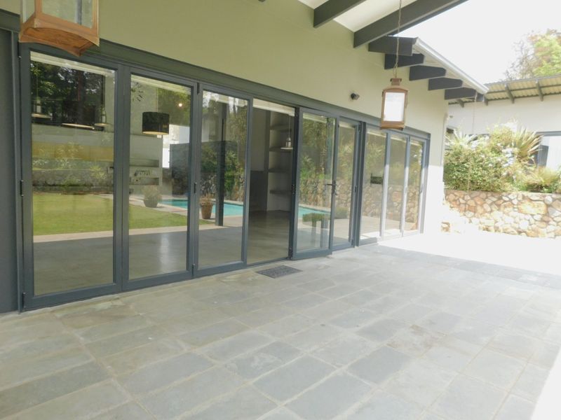 A spacious covered patio featuring stone tile flooring, exposed timber rafters, and large stacking glass doors that provide seamless access to the interior living area.